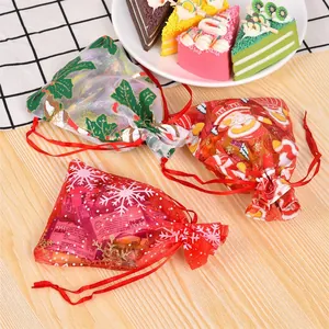 Three Christmas organza drawstring gift bags with snowflake and Santa patterns on wood