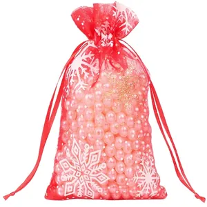 Red organza Christmas drawstring gift bag with white snowflake patterns and ribbon