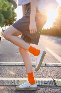 Close-up of bright orange ribbed cotton crew socks paired with white canvas sneakers