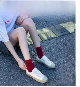 Close-up of white shell-toe sneakers paired with vibrant red ribbed crew socks on asphalt