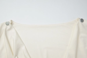 Close-up of off-white top collar with decorative silver metal buttons on shoulders