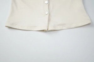 Detailed close-up of cream knit top hem with silver metal buttons and neat stitching