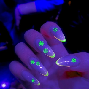Luminous neon green snowflake nail stickers glowing under UV light on almond shaped nails