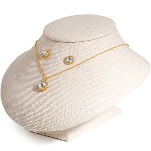 Minimalist gold-plated necklace and zircon stud earrings set on a beige neck display