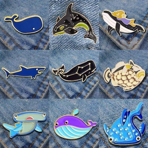 Detailed grid view of nine colorful enamel ocean pins including whales and sharks on denim cloth