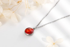 Detail of a silver chain necklace with a red gemstone pendant among white flowers
