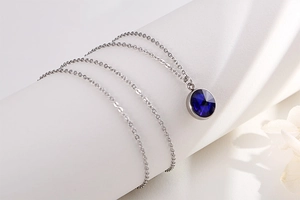 Macro detail of silver necklace featuring a round dark blue faceted gemstone pendant
