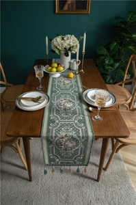 Detailed view of dark green chenille table runner with pink floral patterns and tassels