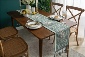 Detailed close-up of green floral chenille table runner with decorative tassels on wood