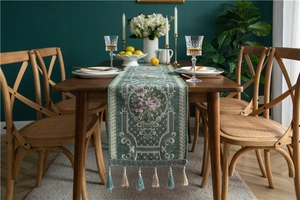 Detail of green chenille table runner with floral embroidery and elegant fringe tassels