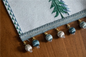 Detailed close-up of Christmas tree embroidery and bicolor ball fringe on white table runner