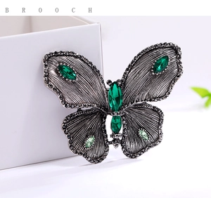 Macro shot of silver butterfly brooch featuring green crystals and detailed engraving