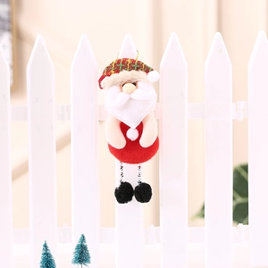 Dettaglio di Babbo Natale in peluche appeso a una staccionata festiva bianca