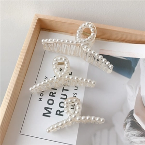 Detailed view of pearl-embellished resin hair claws in three sizes on a wooden tray
