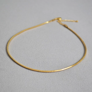 Detailed close-up of a minimalist gold snake bone chain necklace on a grey surface