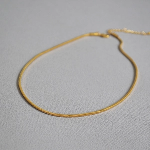 Detail of a sleek gold snake bone chain necklace with a glossy finish on a textured surface