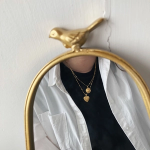 Mirror reflection detail of layered gold coin and heart pendants on a stainless steel chain