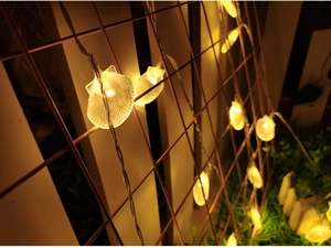 Detail of warm white shell-shaped LED solar string lights on a metal wire mesh