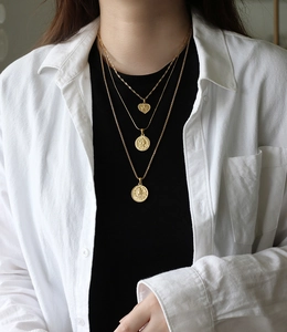 Close-up of a triple layered gold necklace set with heart and coin pendants on a model