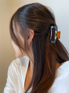 Close-up of a stylish amber and black rectangular hair claw clip worn by a female model