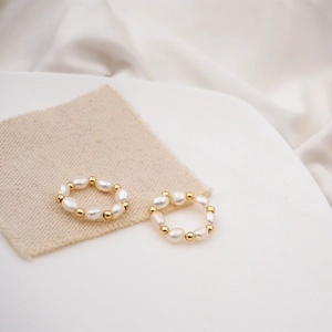 Elegant freshwater pearl elastic rings with gold beads on white textured fabric background