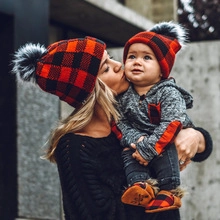 Close-up of matching red and black plaid knit beanies with grey faux fur poms for family
