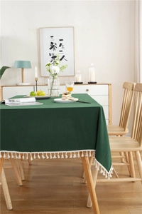 Detail of dark green solid cotton tablecloth featuring elegant white tassel fringe edges