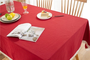 Detail of red cotton tablecloth with white tassel fringe on a rustic wooden dining table