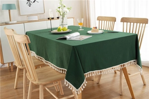 Detail of green washed cotton tablecloth with white tassel edge on wooden table