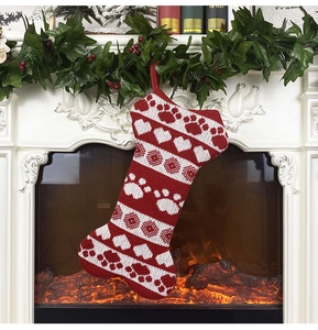 Detail of red and white bone-shaped knitted Christmas stocking with paw prints by a fireplace