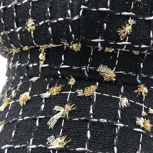 Close-up of black tweed fabric texture with gold accents and grid pattern on the hat