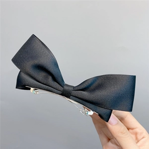 Detailed close-up of a black satin bow hair clip showing silk texture and metal spring