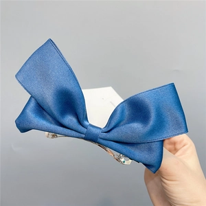 Detail showing hand holding blue satin bow hair clip with a metal spring fastener