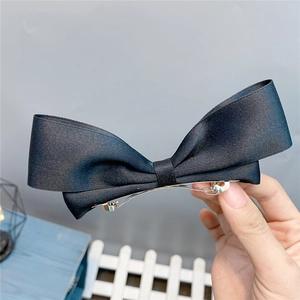Detailed view of a black satin bow hair clip with silver metal spring fastener held in hand