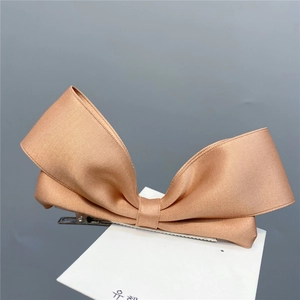 Macro detail of the elegant pink satin bow hair clip with a smooth metallic duckbill grip