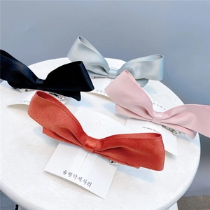 Detailed view of four satin bow hair clips in black, grey, pink, and orange on a stool