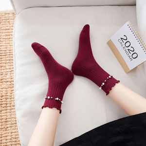 Dark red crew socks with ruffle edges and pearl accents on a model in a cozy setting
