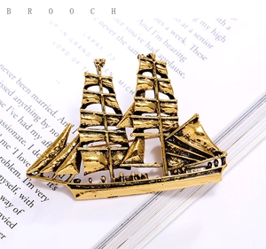 Macro detail of vintage gold sailing boat brooch with intricate mast texture on book