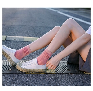 Close-up of pink ribbed cotton socks worn with white canvas shoes on a road surface