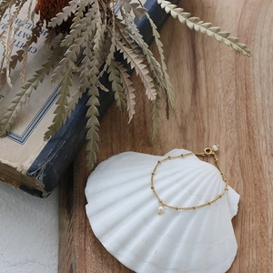 Detail of 18K gold-plated titanium chain bracelet with delicate freshwater pearls on a shell