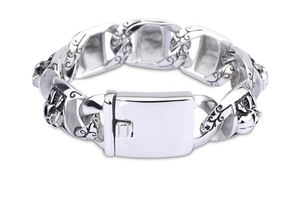 Detailed close-up of punk skull engraving and thick silver Cuban link chain bracelet