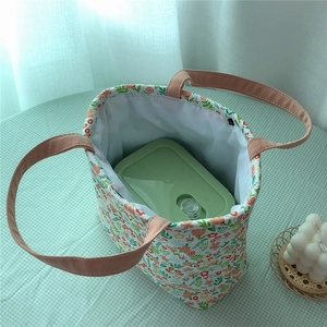 Floral lunch bag with pink handles showing a green bento box inside on a plaid mat