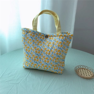 Detailed view of floral canvas lunch bag with yellow handle and metal button closure