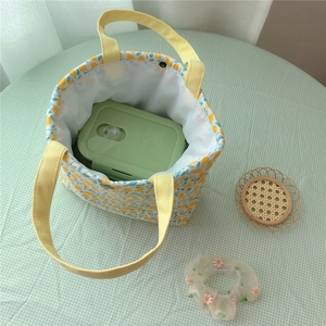 Detail of floral lunch bag with yellow handle, holding a green bento box on plaid cloth