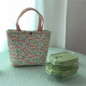 Floral lunch bag with pink handles next to glass food containers on a green tablecloth