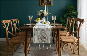 Close-up of beige chenille table runner with floral embroidery, lace trim and tassels