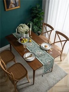 Detail of vintage floral table runner with tassels on a wooden dining table