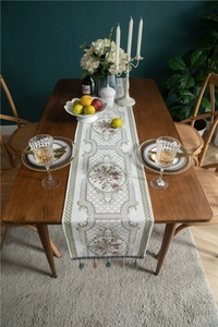 Close-up of elegant beige chenille table runner with rose embroidery and fringe tassels
