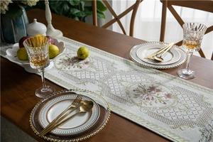 Close-up of beige chenille table runner with pink floral embroidery and gold tassel