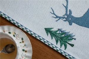 Detail of blue deer and green tree embroidery on chenille table runner with tassels